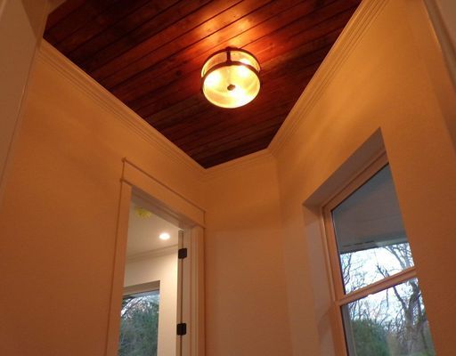 A brightly lit indoor entryway featuring a warm, dark wood-paneled ceiling, a central dome light, and a large window.