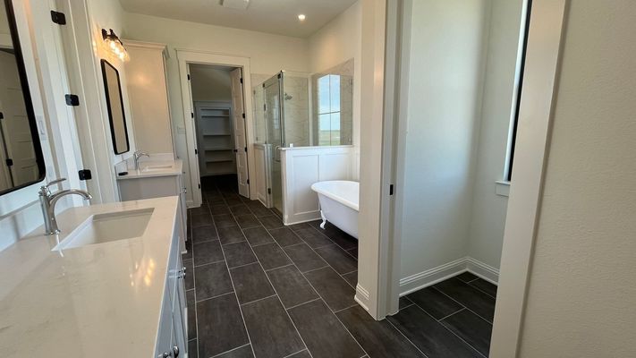 Modern bathroom with a white vanity, a standalone soaking tub, walk-in shower, and dark tiled floors.