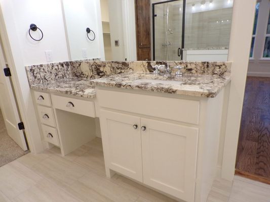 A bathroom vanity with white cabinets and a beige-patterned stone countertop, featuring a sink and mirror.