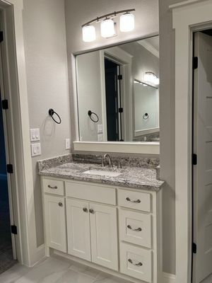 A white bathroom vanity with a speckled countertop and three-light fixture under a mirror in a modern gray room.