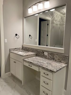 A bathroom vanity with a granite countertop, white cabinets, and a four-light fixture above a large mirror.