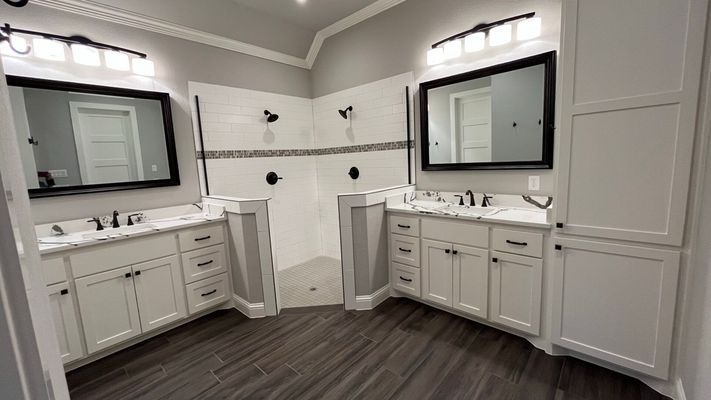 A modern bathroom with two white vanities, black-framed mirrors, and a central walk-in shower with tiled walls.
