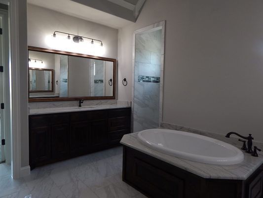A bathroom with a dark wood vanity, a large mirror, a marble-topped soaking tub, and a glass-enclosed shower.