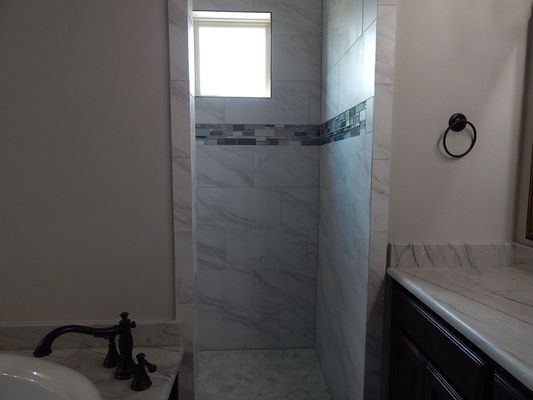 A walk-in shower with white marbled walls, a decorative mosaic tile stripe, and a small square window.