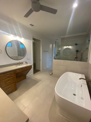 A modern bathroom with a white freestanding tub, wood vanity, round mirror, and a glass-enclosed shower.