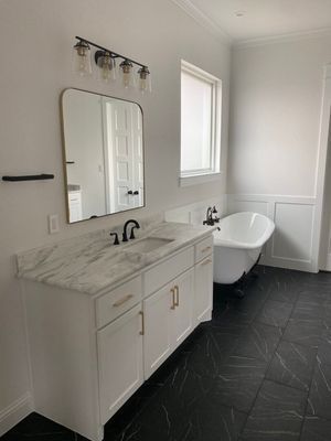 A modern bathroom with a white marble vanity, gold hardware, a rectangular mirror, and a standalone tub on black tile.
