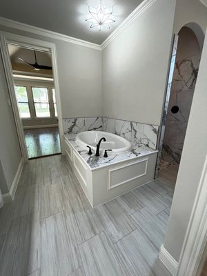 A bathroom featuring a white oval tub set in a marble surround, grey tiled floors, and a walk-in shower.