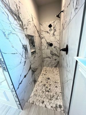 Modern walk-in shower with white-and-black marble tile walls, a hexagonal tile floor, and black fixtures.