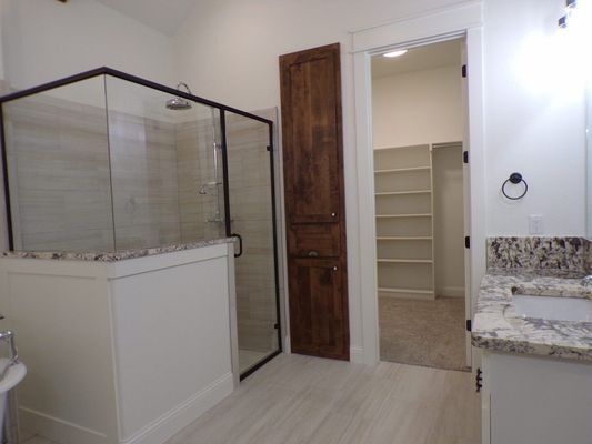 A modern bathroom featuring a glass-enclosed shower, a tall wooden storage cabinet, and a walk-in closet with shelving.
