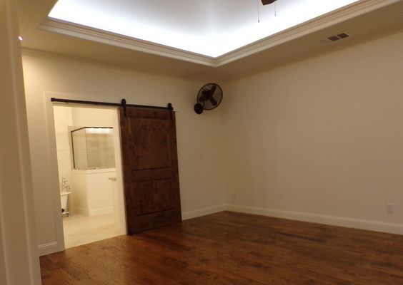 A room with hardwood floors, a tray ceiling with recessed lighting, a wooden barn door, and a wall-mounted industrial fan.