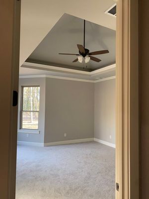 A bedroom interior viewed from a doorway, featuring beige walls, gray carpeting, and a recessed ceiling with a fan.