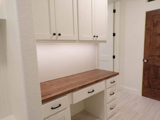 Built-in white cabinets and drawers with a wooden desktop and under-cabinet lighting in a bright, neutral room.