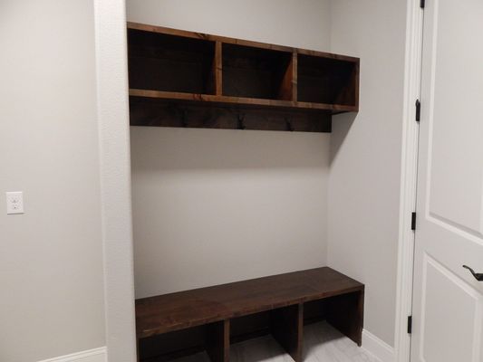 A built-in mudroom bench with three lower storage cubbies and a matching upper shelf with coat hooks on a neutral wall.