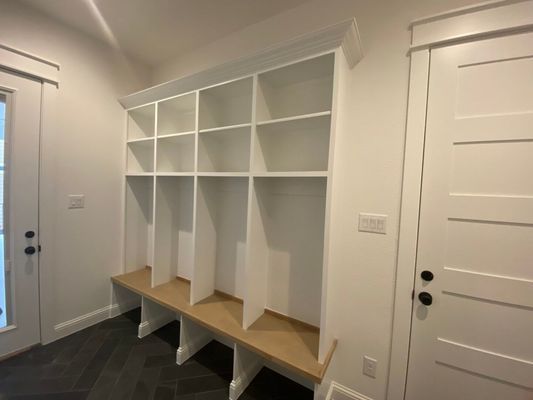 A white, four-section mudroom built-in unit with upper shelving and wood-tone bench seating.