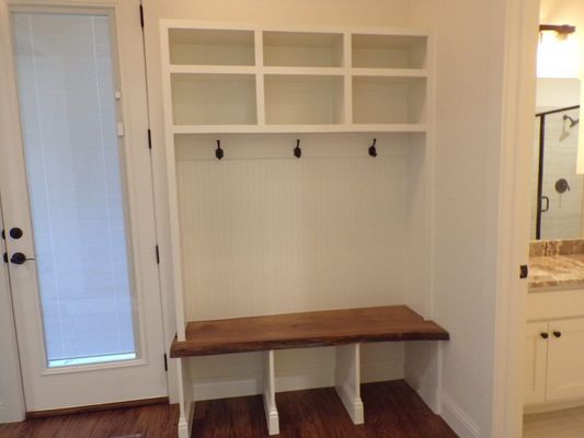 A white mudroom bench with a dark wood seat, top storage cubbies, and coat hooks, positioned next to a glass-paned door.