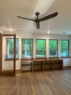 A room with a wooden ceiling fan, light wood floors, a glass-paneled door, and a built-in low wooden shelf under windows.