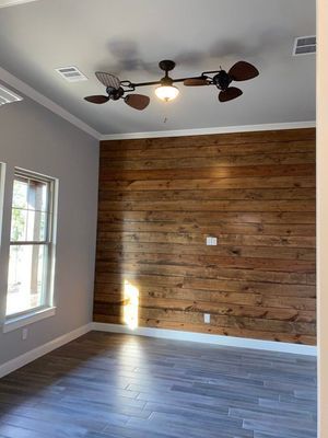 An empty room with gray walls and flooring, featuring a wood-plank accent wall and a unique multi-bladed ceiling fan.