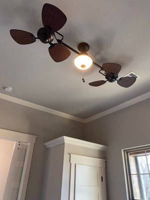 A dual-headed, bronze-colored ceiling fan with a central light fixture, mounted on a white ceiling in a room.