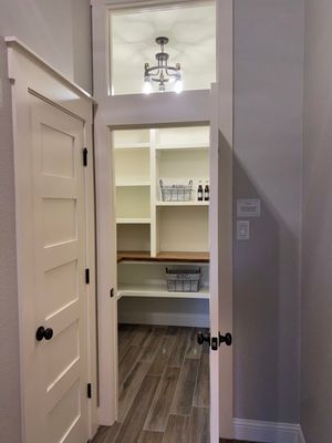 A pantry with white shelving, a wood counter, and a glass-paneled transom door with black hardware.