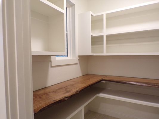A pantry featuring white built-in upper shelving and a lower countertop made of raw-edge natural wood.