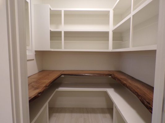 A pantry with white shelves and a central counter featuring natural, live-edge wood surfaces.