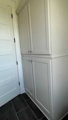 Tall, light gray storage cabinet with four doors stands next to a matching white interior door on dark tiled flooring.