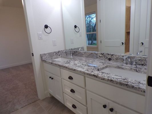 A double-vanity bathroom featuring white cabinets, a speckled granite countertop, dual sinks, and a large wall mirror.