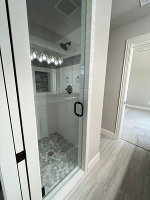 A modern walk-in shower with white subway tiles, a stone pebble floor, and a glass door, adjacent to an open doorway.