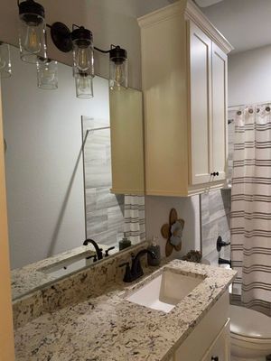 A bathroom vanity with speckled granite countertops, a dark faucet, a large mirror, wall lighting, and a white cabinet.