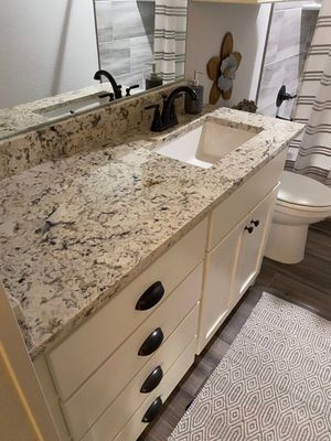 A bathroom vanity with speckled granite countertop, white cabinets, oil-rubbed bronze fixtures, and a white sink.