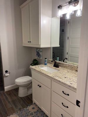 A small bathroom featuring a white vanity with granite countertops, a wall cabinet, a mirror, and a toilet on wood flooring.