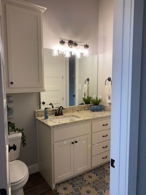 A bright bathroom with white cabinets, speckled granite countertops, dark fixtures, and patterned tile flooring.