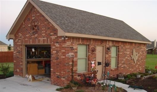 A small brick detached garage with a gable roof, an open doorway, two windows, and a decorative star on the side wall.