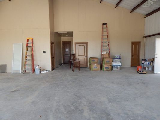 Interior of a warehouse with concrete floors, two wooden ladders, a few doors, and cardboard boxes.