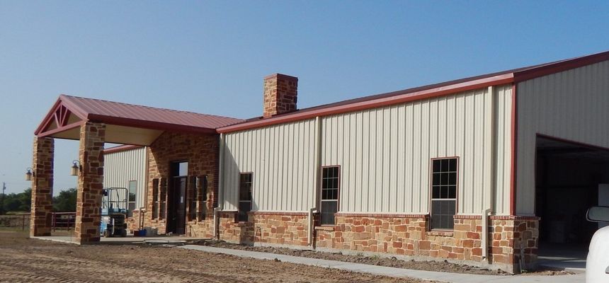 Single-story metal building with a tan exterior, stone accents, a brick chimney, and an attached covered entryway.