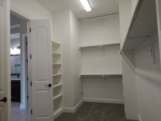 A walk-in closet with white walls, gray carpet, built-in wooden shelves, and wire hanging racks.