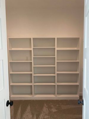 A set of built-in, off-white open shelving units with five shelves each, viewed through a doorway.