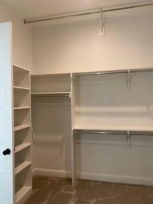 Empty walk-in closet with white walls, beige carpet, built-in shelving, and hanging rods.