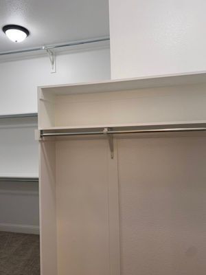 A white closet organizer with a built-in shelf and a metal clothing rod, situated in a room with a light fixture above.