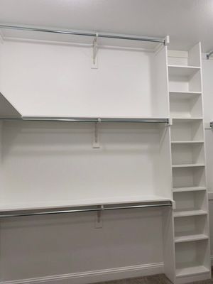 A white closet organizer featuring two horizontal hanging rods with shelves above and a tall shelving unit on the right.
