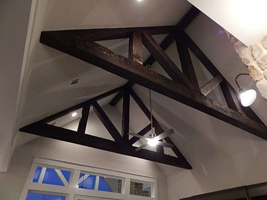Dark wooden trusses frame a vaulted ceiling with recessed lighting and a ceiling fan in a brightly lit room.