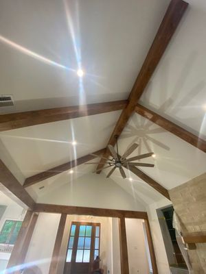 A high, white vaulted ceiling features exposed dark wooden beams and a large ceiling fan with a stone wall in the corner.