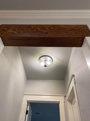 A hallway with white walls and trim, featuring a prominent stained wood faux beam on the ceiling near a round light.