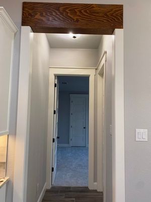 A hallway viewed through a doorway with a dark wood header, leading to a room with a white door and gray carpet.