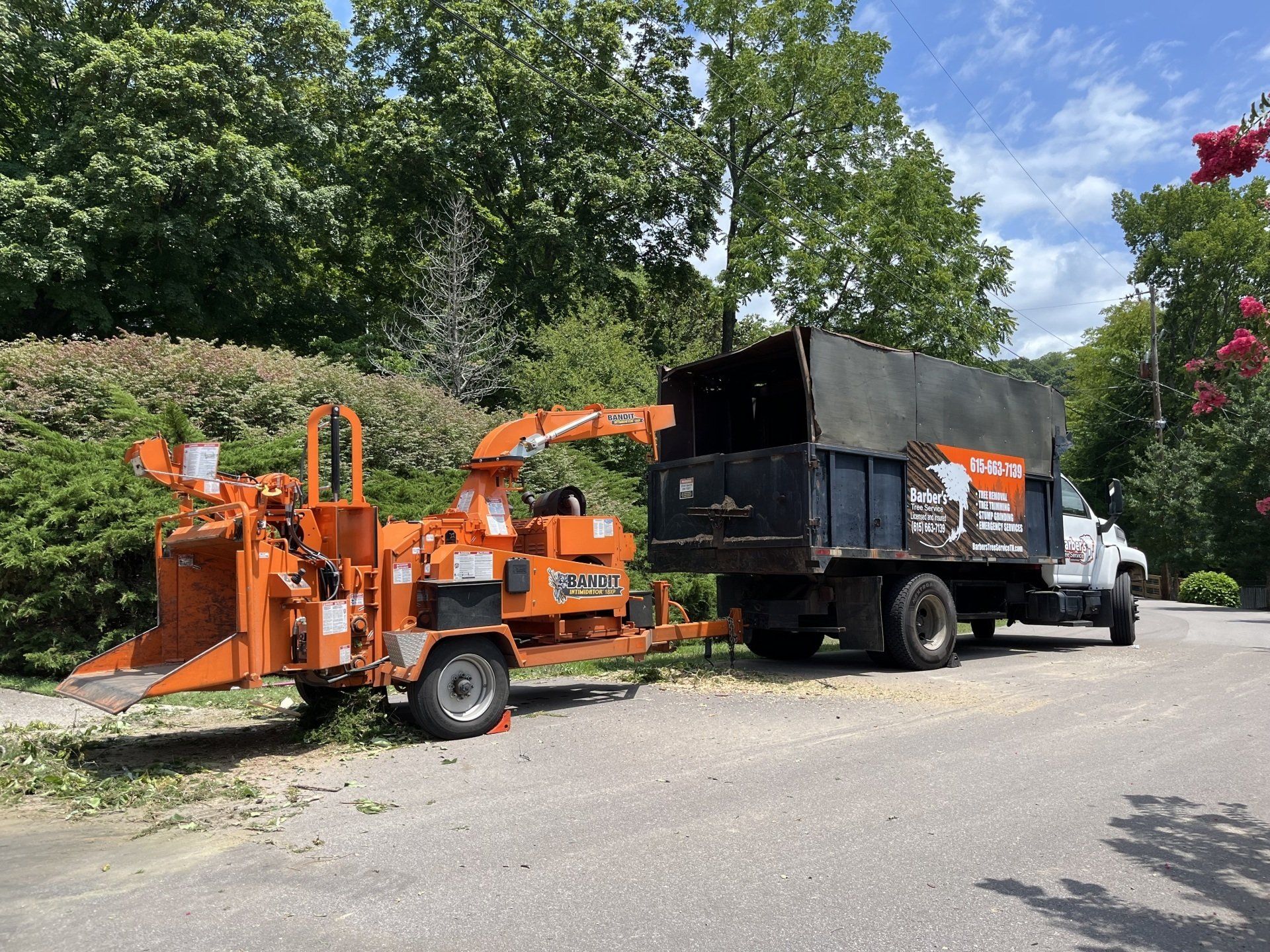 A tree chipper is parked next to a dump truck.