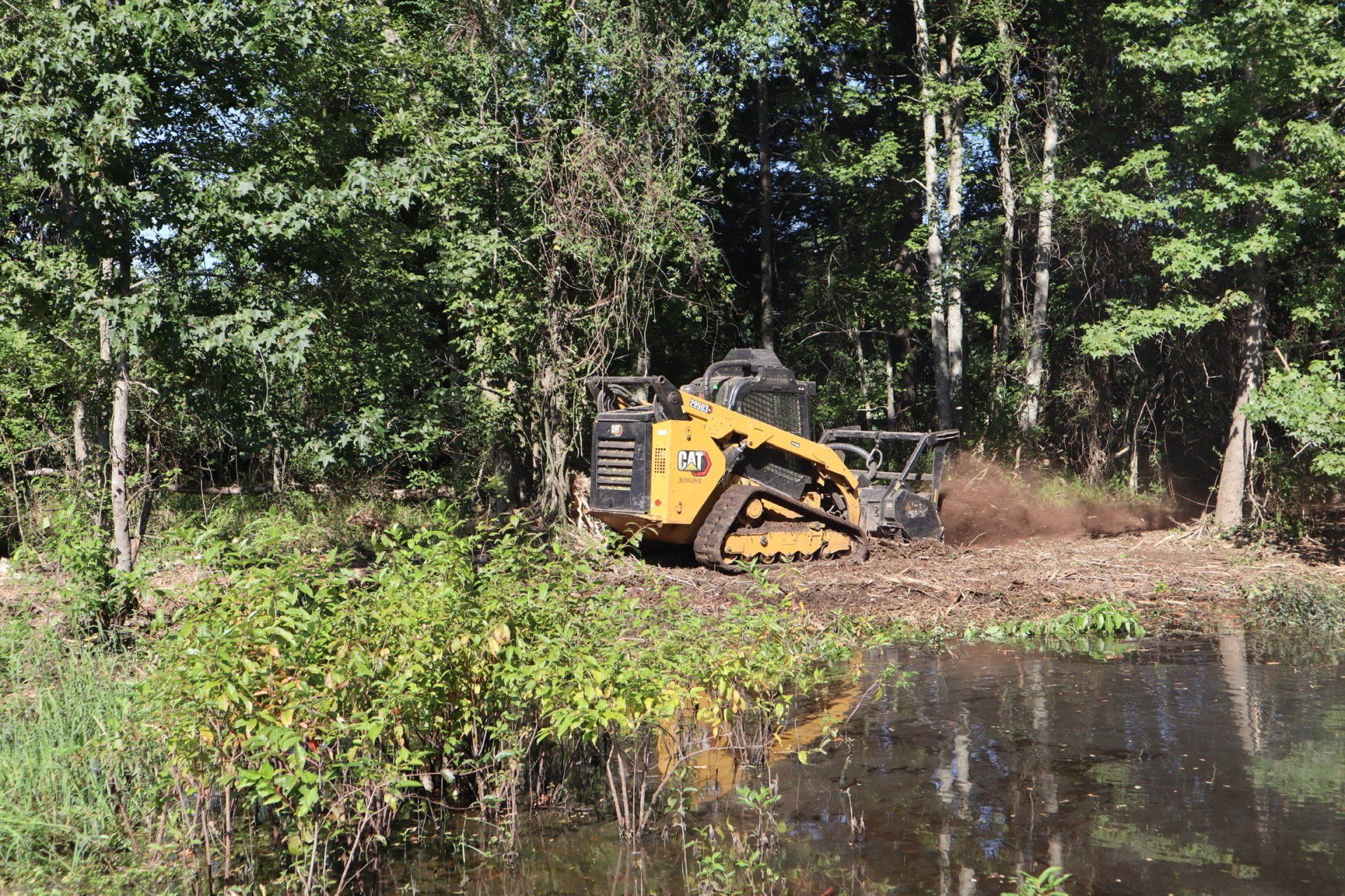 A bulldozer is clearing a pond in the woods.