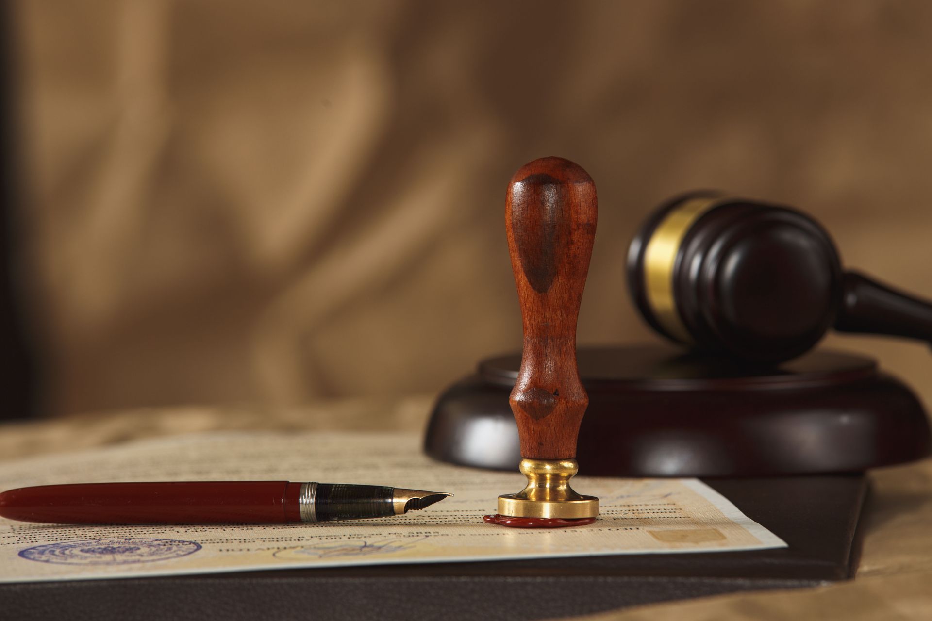 A legal document with a fountain pen, a wooden wax seal stamp, and a judge's gavel on a dark surface.