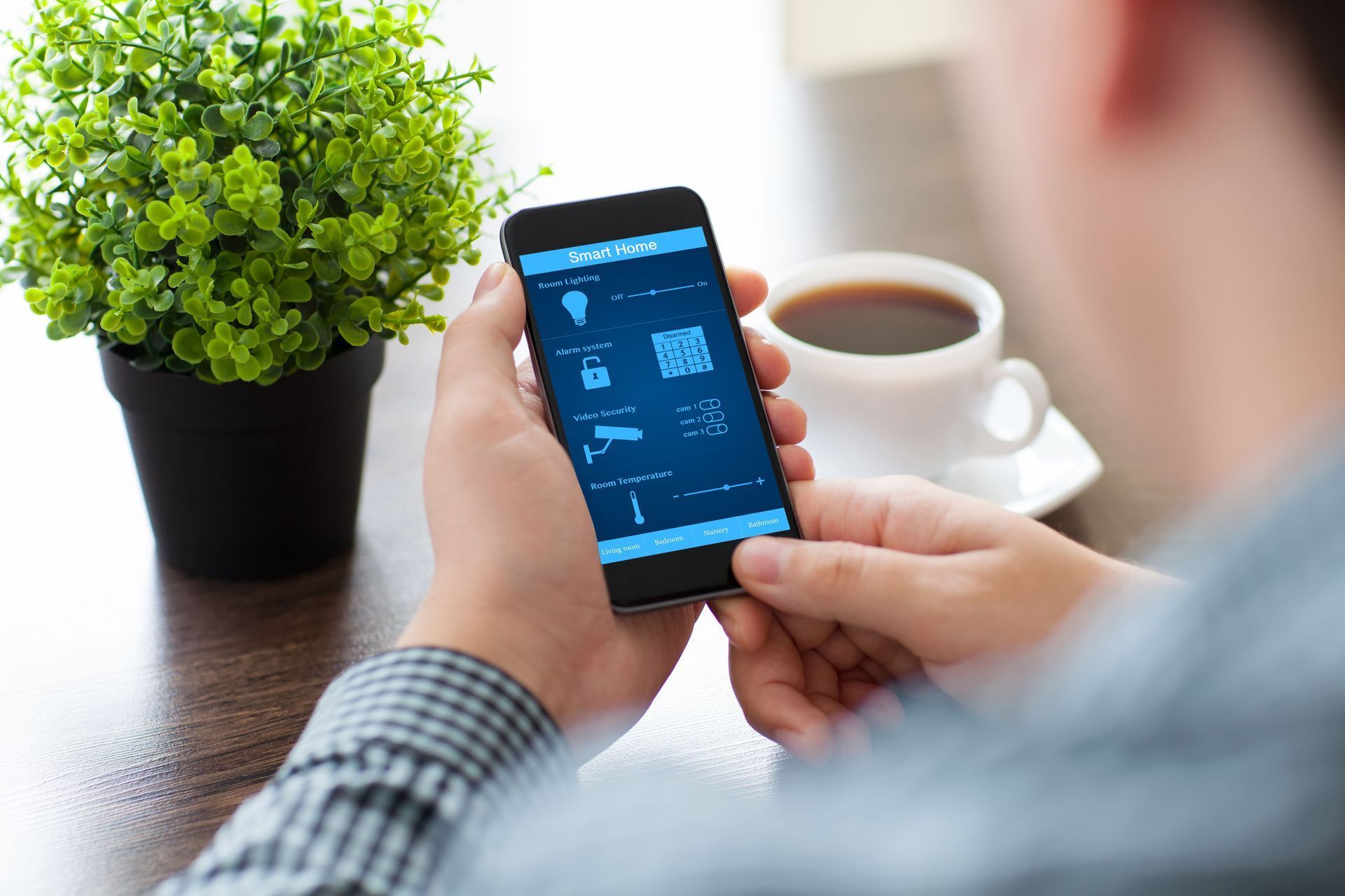 Person using a smartphone beside a potted plant and coffee cup on a table