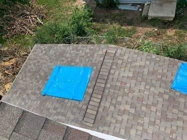 An aerial view of a roof with two blue tarps on it.