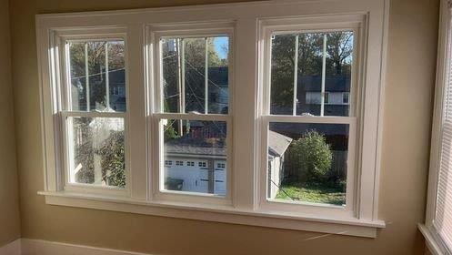 A room with three windows and a view of a house.
